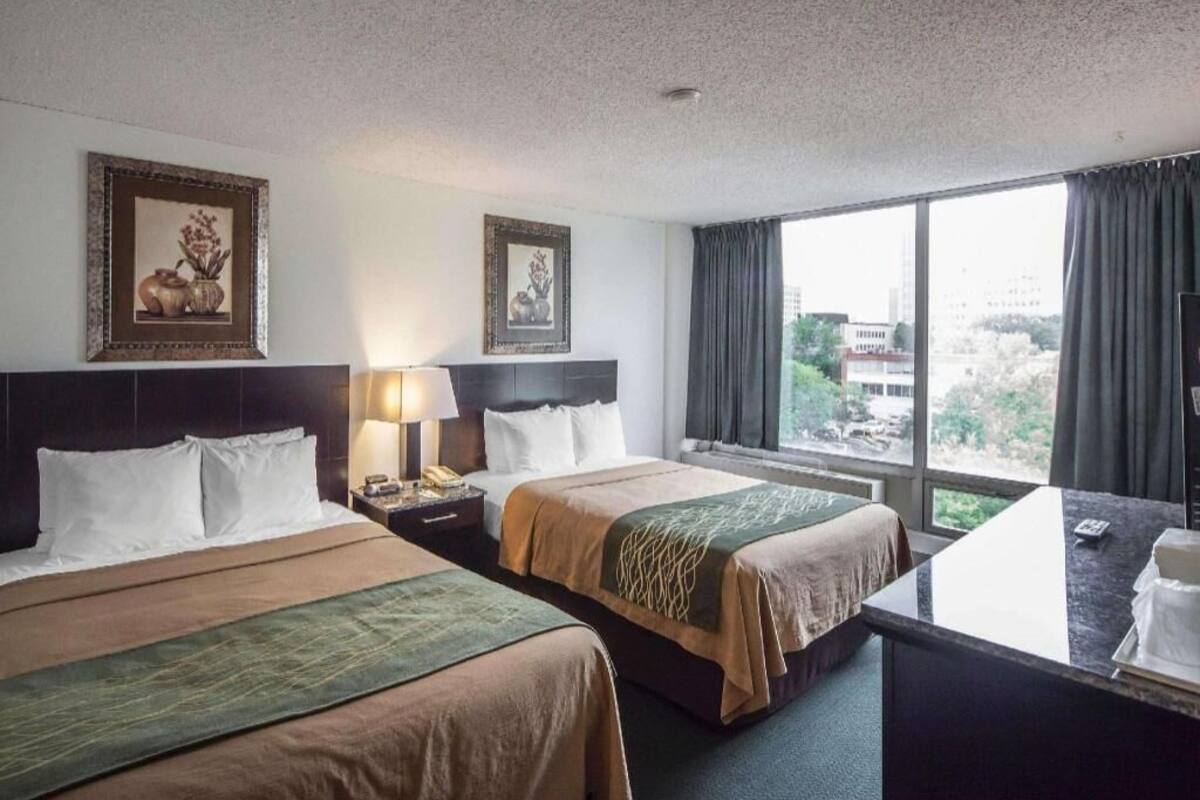 Habitación de hotel con dos camas, un escritorio y un ventanal con vistas.