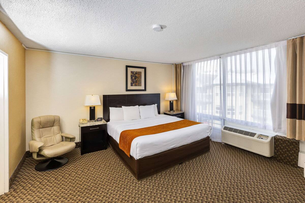 Una habitación de hotel con una cama grande, una silla, un escritorio y una ventana con cortinas.