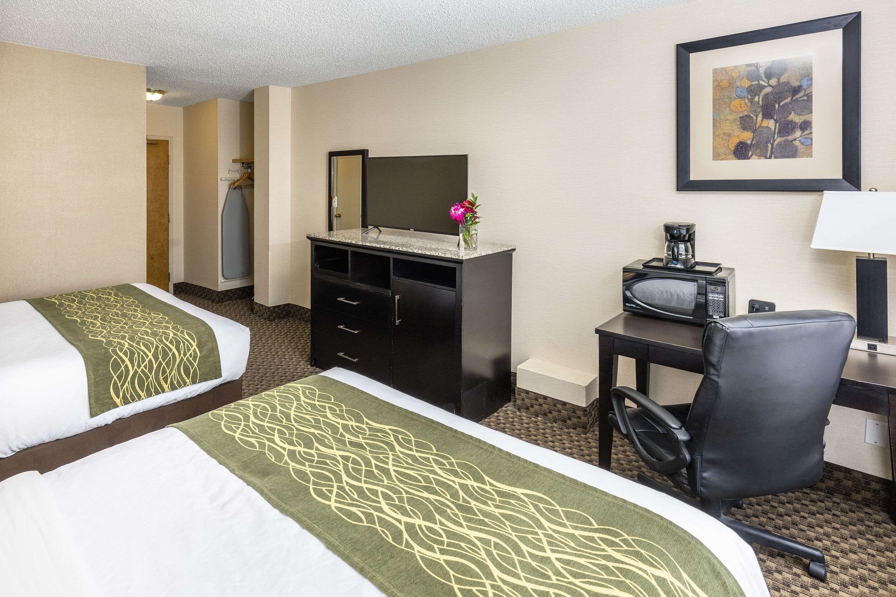Habitación de hotel con dos camas, un escritorio con silla, cómoda, espejo, un cuadro en la pared y cafetera.