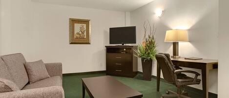 Habitación de hotel con sofá, televisión, escritorio con silla, lámpara y planta.