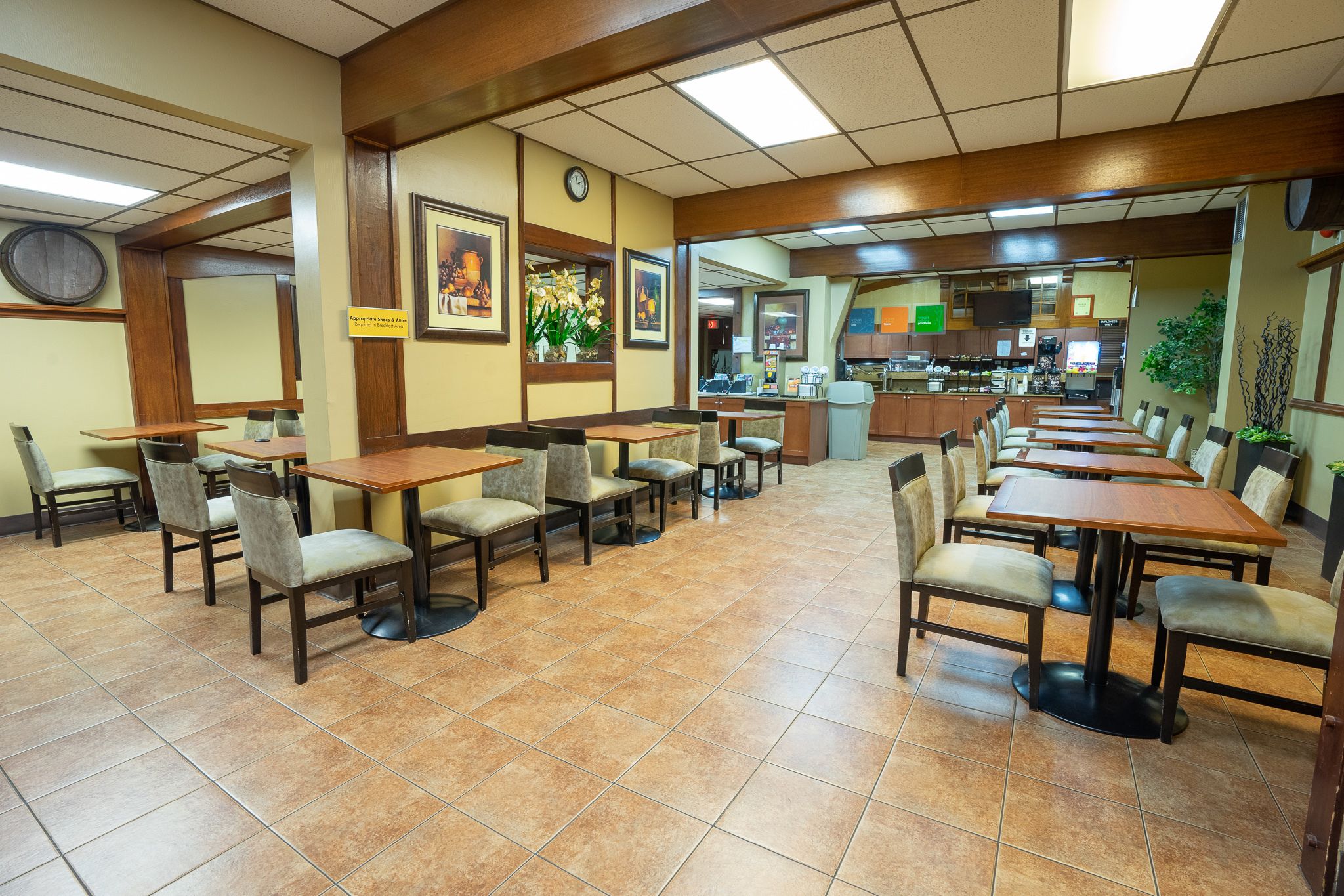 Un restaurant avec plusieurs tables et chaises, une cuisine visible à travers une porte ouverte, et une horloge au mur.