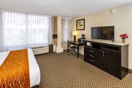 A hotel room with a bed, desk, TV, and a window with curtains.