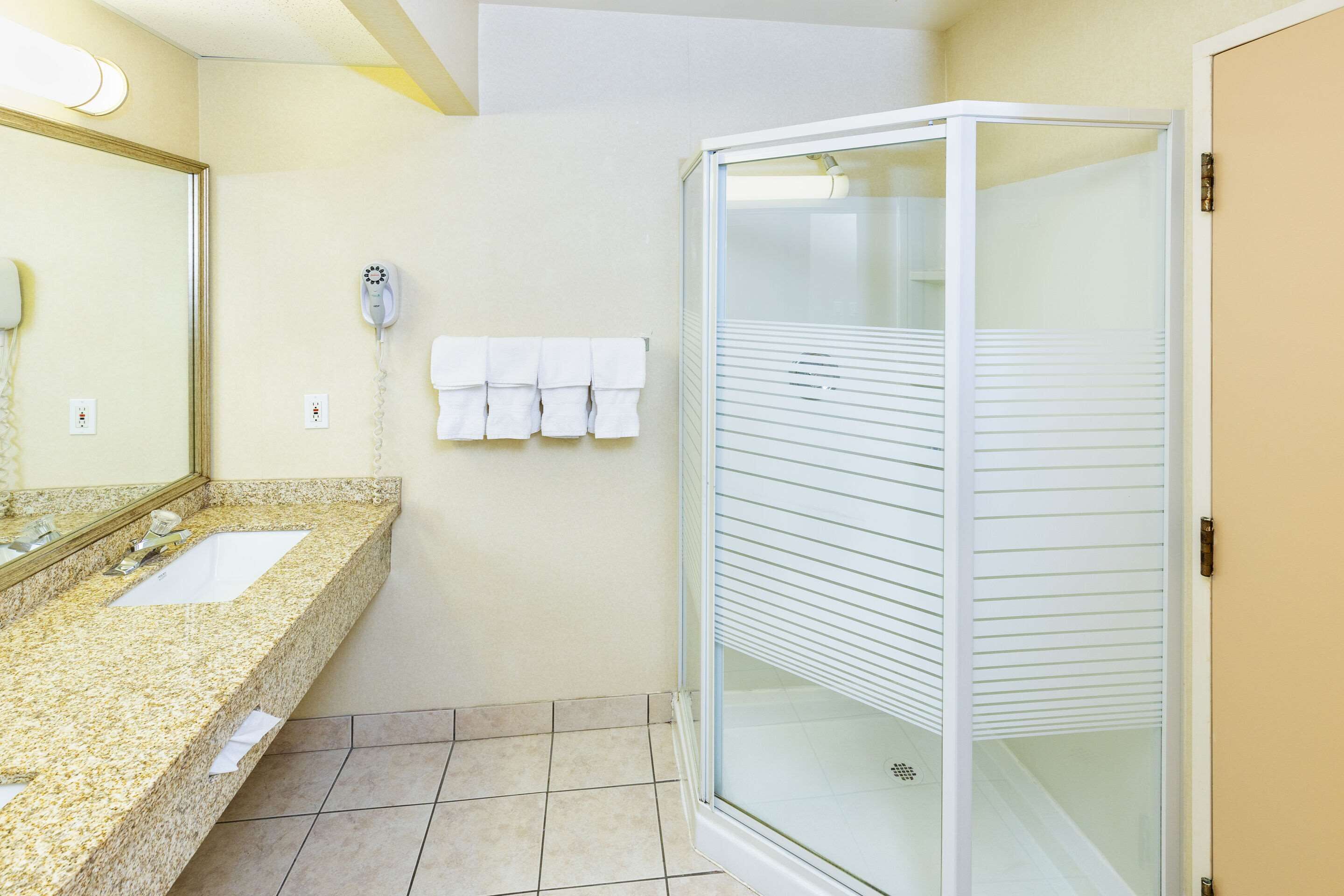 A bathroom with a granite countertop, two sinks, a glass shower enclosure, and a towel rack with multiple towels.