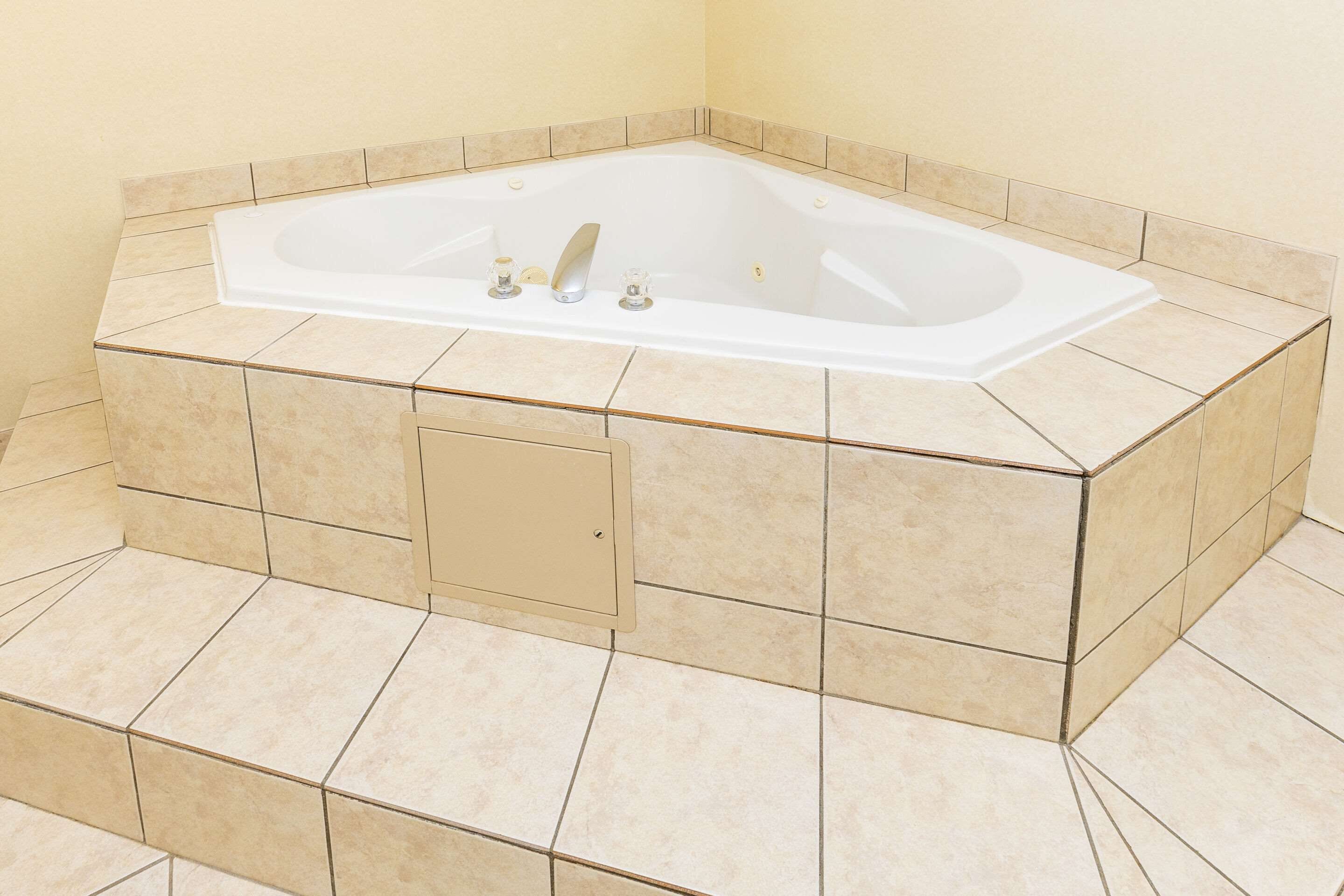 Une baignoire d’angle avec un panneau de douche intégré, des carreaux de couleur beige et un mur de couleur neutre.
