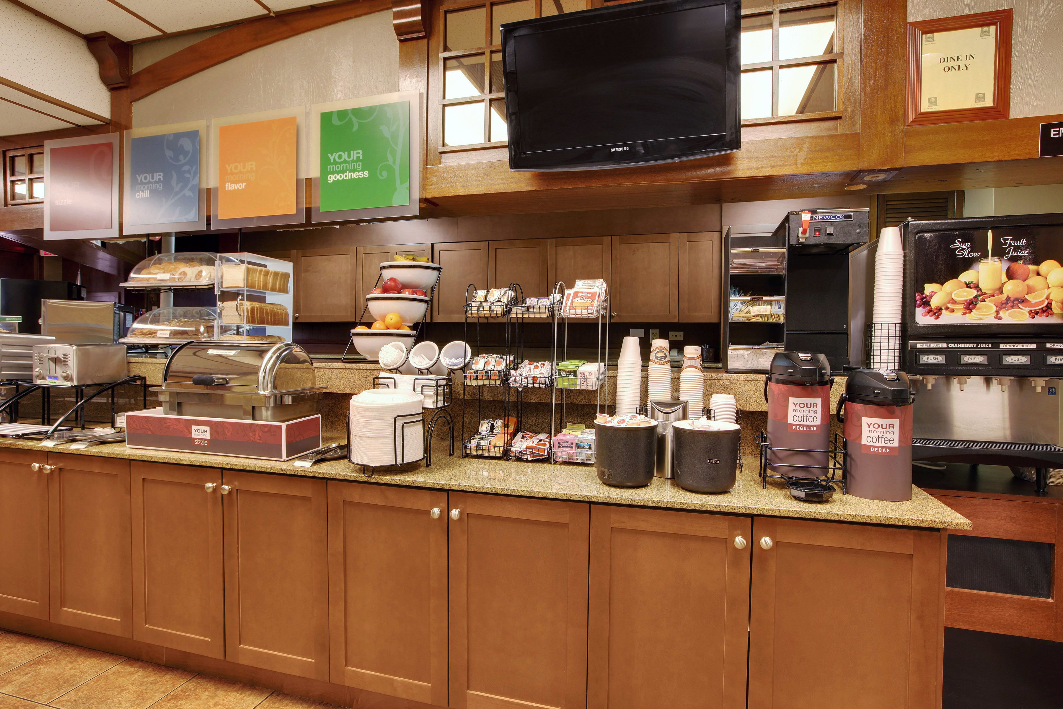 Un espace pour le petit-déjeuner à l’hôtel, avec un buffet où les clients peuvent se servir eux-mêmes, des distributeurs de café et un réfrigérateur pour les jus de fruits.