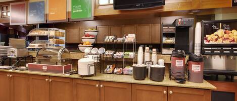 A hotel breakfast area with a self-serve station, coffee dispensers, and a fruit juice cooler.