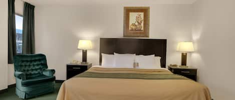 A hotel room with a large bed, two bedside tables with lamps, a green armchair, and a framed picture on the wall.