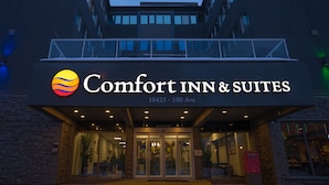 The exterior of Comfort Inn & Suites, featuring a prominent sign with the hotel name and address, a glass entrance, and a balcony above the doors. - Comfort Inn & Suites Edmonton Downtown (Edmonton)