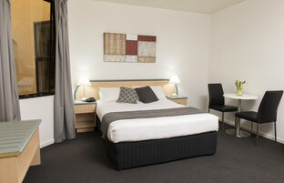Habitación de hotel con cama, mesitas de noche, escritorio, dos sillas, una mesita pequeña y una obra de arte en la pared.