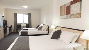 Une chambre d’hôtel avec deux lits, un bureau avec une chaise, une télévision et une fenêtre avec des rideaux.