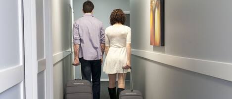 A narrow hallway with grey carpet, white walls, and a painting on the right.