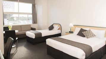 A hotel room with two beds, a sofa, a desk, and a window with curtains.