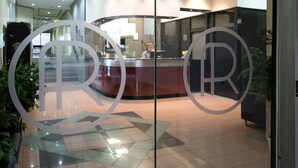 Un espace d’accueil doté d’une cloison en verre, une réceptionniste derrière celle-ci, et un aménagement intérieur moderne.