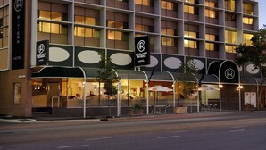 Un hôtel à plusieurs étages doté d’une façade moderne, de nombreux balcons et d’un restaurant situé au rez-de-chaussée, avec une terrasse.