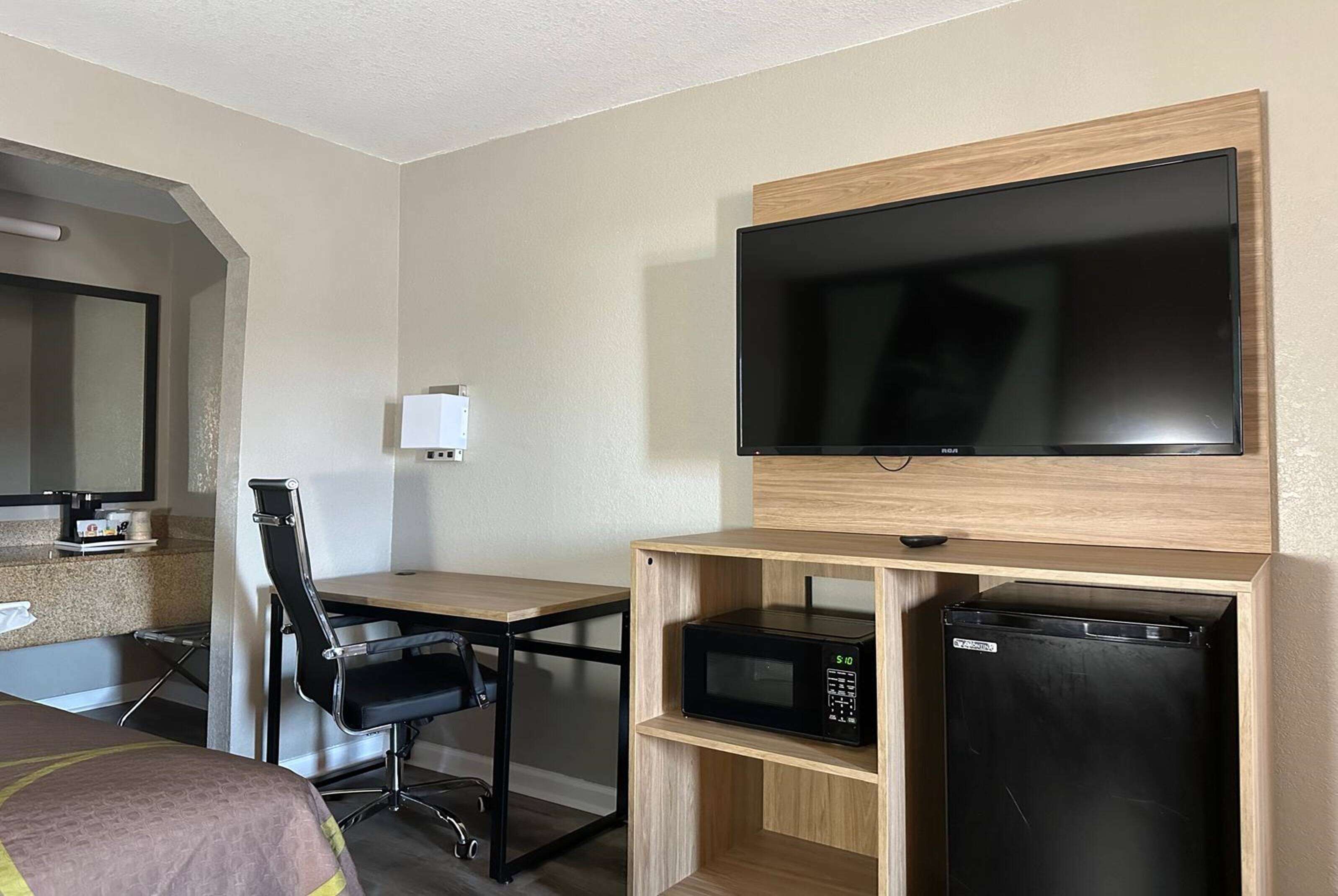 Habitación de hotel con cama, escritorio, silla, televisor, microondas y refrigerador.