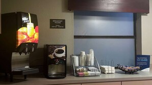A breakfast station with a fruit juice dispenser, coffee machine, and neatly arranged plates and napkins. - Super 8 by Wyndham Monroe (Monroe)