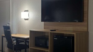 A room with a flat-screen TV mounted on the wall, a wooden desk with a chair, and built-in appliances including a microwave and a mini-fridge. - Super 8 by Wyndham Monroe (Monroe)