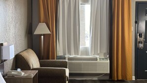 A hotel room with a bed, a chair, a desk with a lamp, a telephone, and an air conditioning unit. - Super 8 by Wyndham Monroe (Monroe)