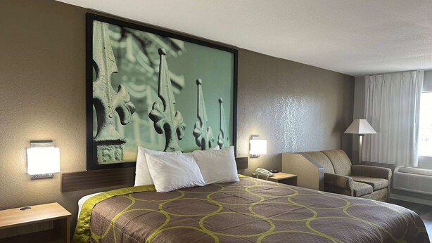 A hotel room with a large bed, a headboard with a painting, a desk with a lamp, a chair, and a window with curtains. - Super 8 by Wyndham Monroe (Monroe)