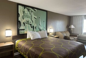 Una habitación de hotel con una cama grande, cabecera con un cuadro, un escritorio con lámpara, una silla y una ventana con cortinas.