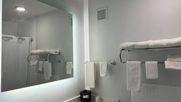 A bathroom with a large mirror, a sink with a towel rack, and a shower area.