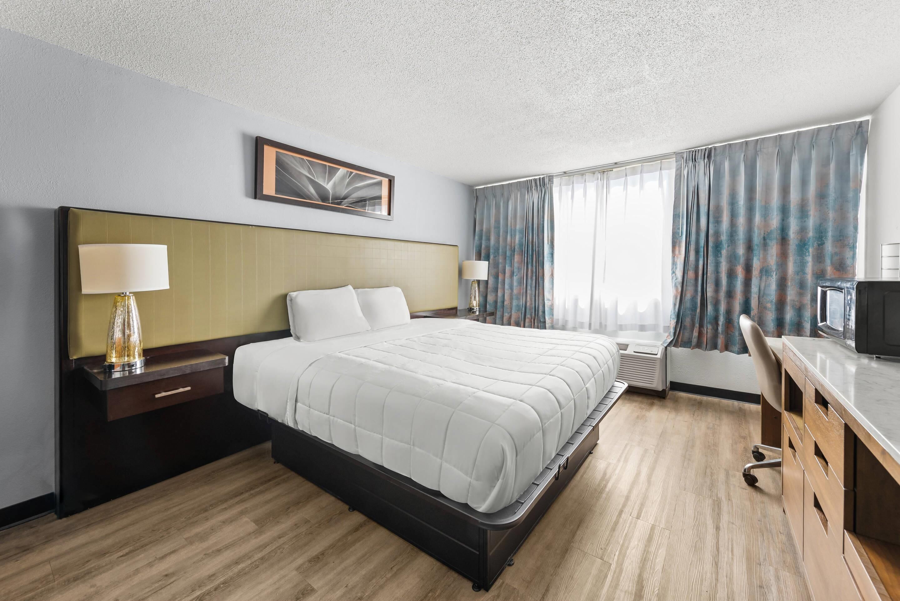Una habitación de hotel con una cama grande, un escritorio con una silla, un televisor y una ventana con cortinas.