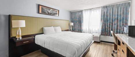 Una habitación de hotel con una cama grande, un escritorio con una silla, un televisor y una ventana con cortinas.