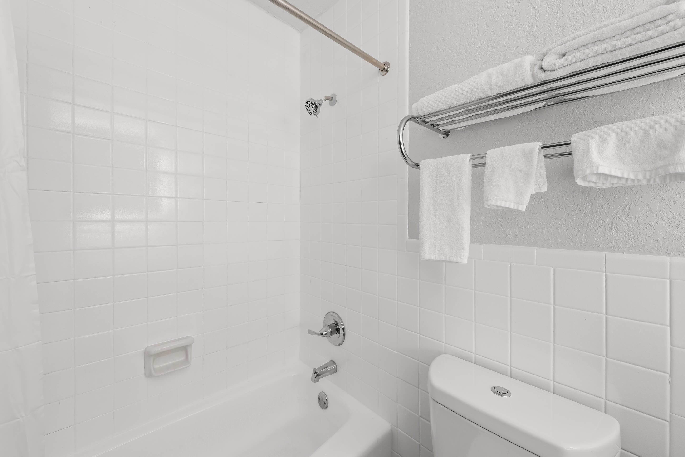 Un baño moderno con pared de azulejos blancos, una bañera, un inodoro y un perchero con toallas dobladas con cuidado.