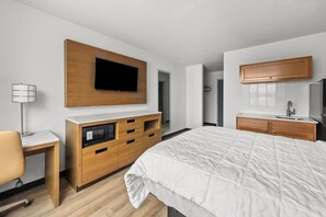 Un dormitorio moderno con una cama grande, cómoda de madera, televisor integrado y escritorio con lámpara.