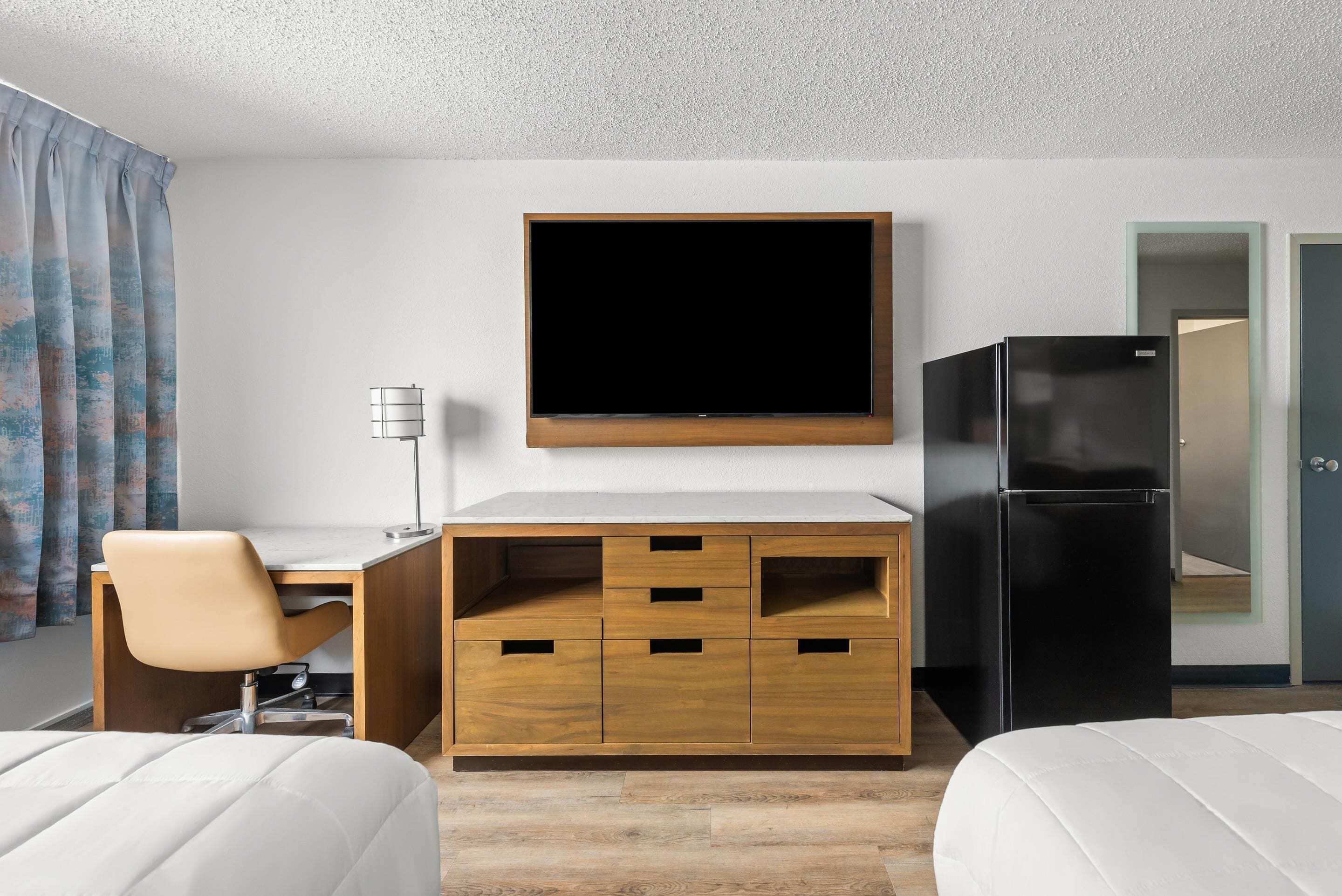 Ein Hotelzimmer mit Bett, Schreibtisch mit Stuhl, Flachbildfernseher, Kühlschrank und Kleiderschrank.