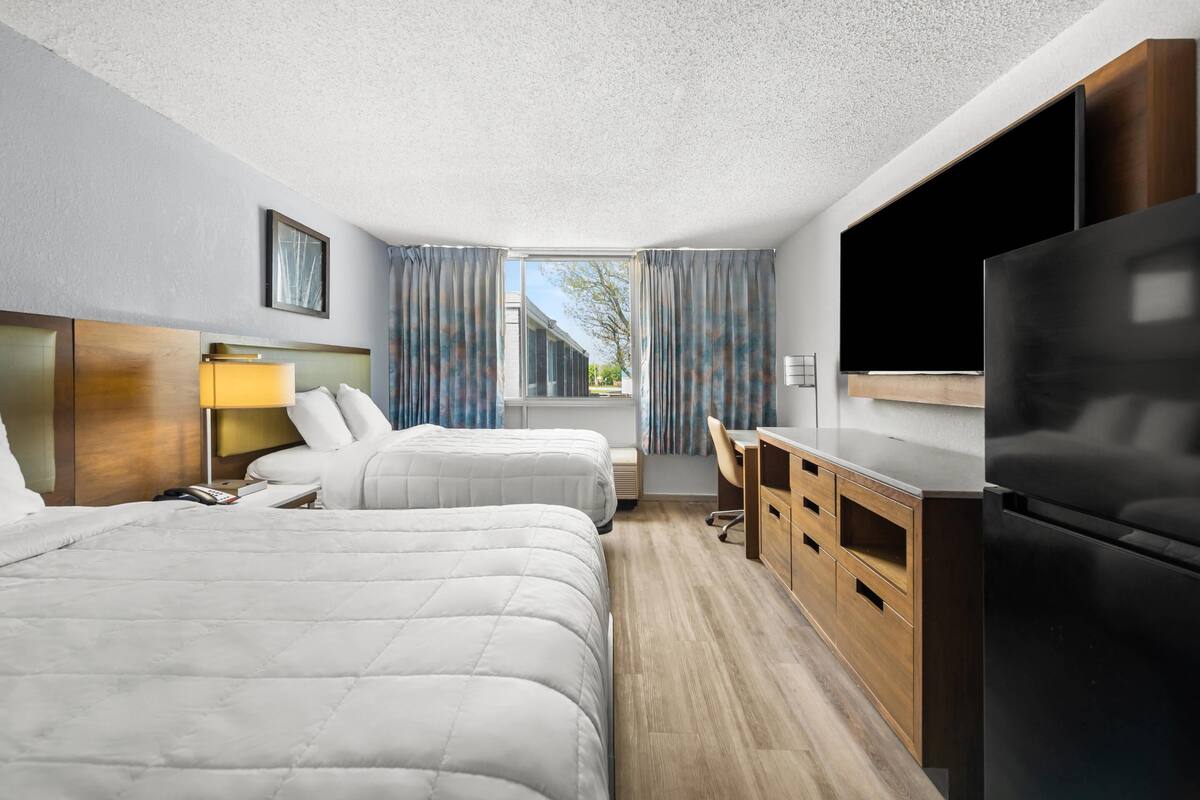 A hotel room with two beds, a desk, a TV, and a refrigerator.