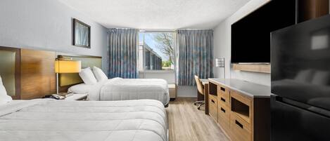 Habitación de hotel con dos camas, un escritorio, televisor y refrigerador.