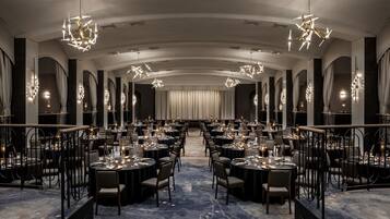 Un comedor formal con varias mesas, elegantes candelabros y un largo pasillo que conduce a una zona cubierta por cortinas.