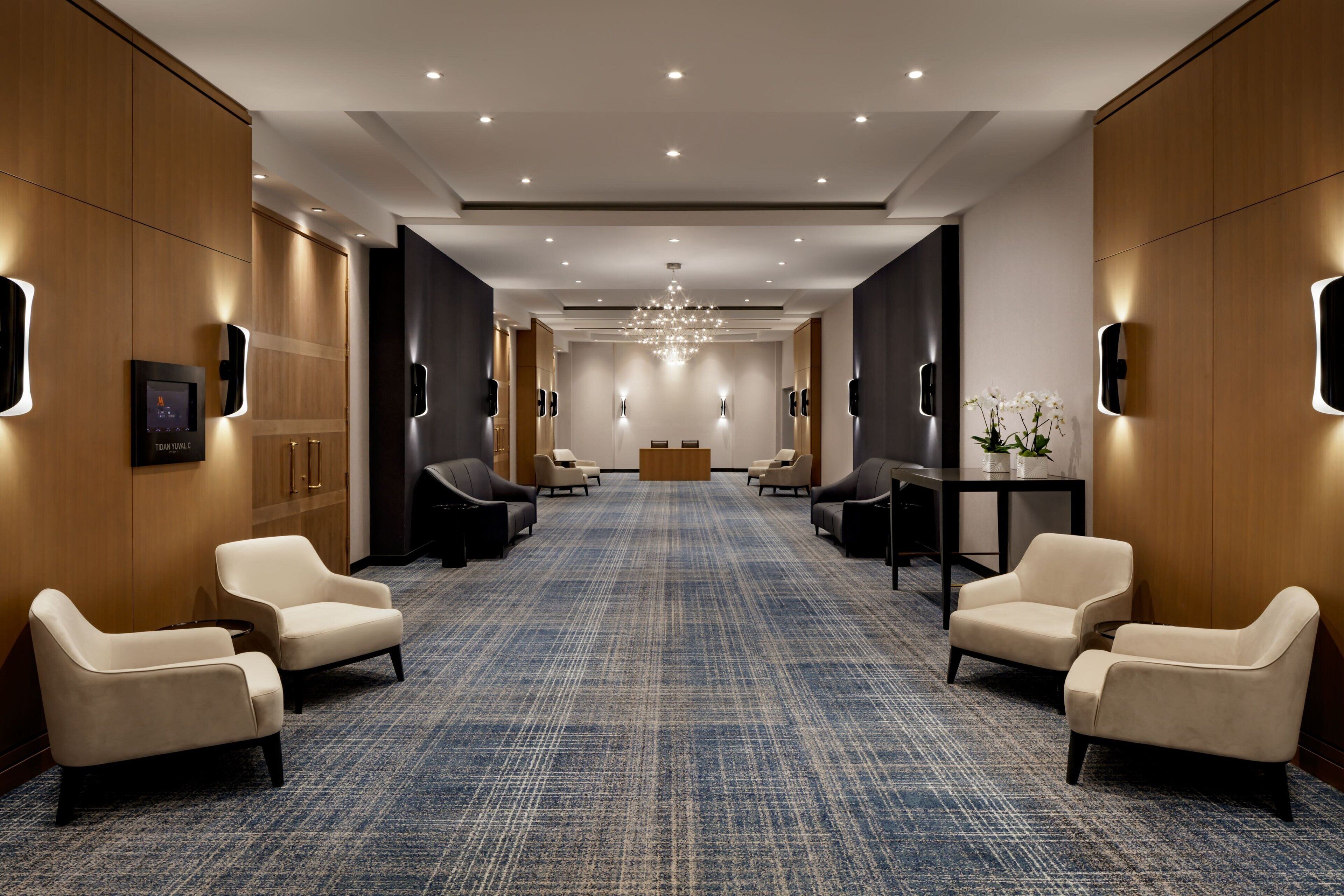 Eine Hotellobby mit blauem Teppich, einer Sitzecke mit Stühlen, einem Empfangstresen und einer Kristallleuchter.