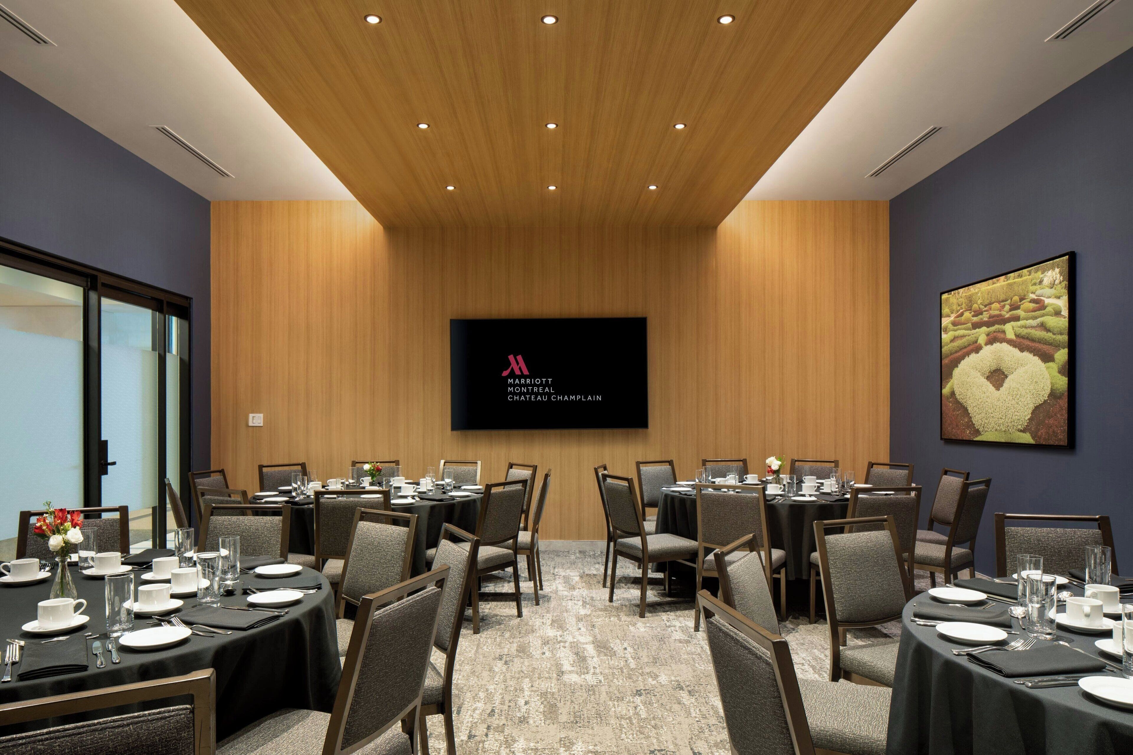 A conference room with round tables, chairs, and a large screen displaying the Marriott logo.