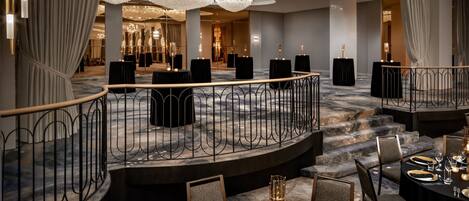 Un comedor de hotel lujoso con suelo de mármol, elegantes candelabros y vistas al salón de banquetes contiguo.