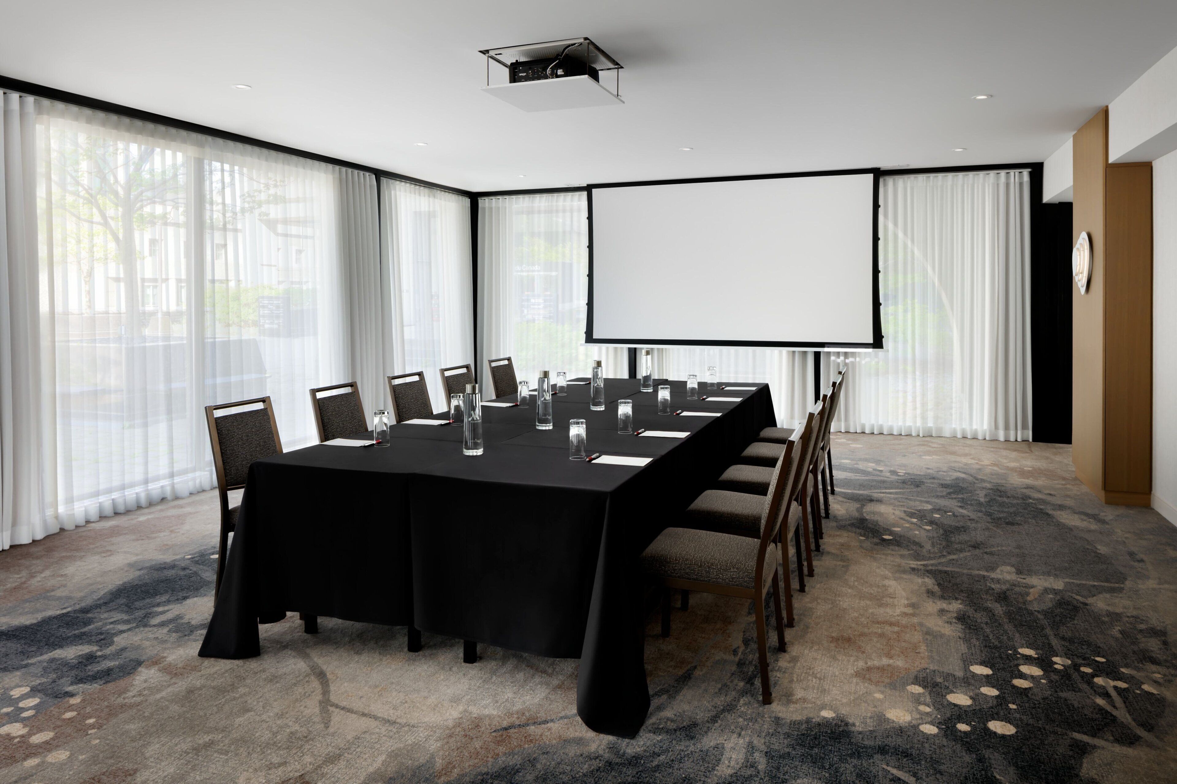 Ein Konferenzraum mit großem Tisch, Stühlen, einer Projektionsleinwand und Teppichboden.