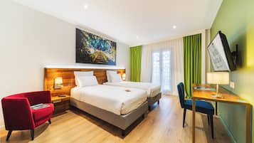 Una habitación de hotel con cama, escritorio, silla, mesita de noche, lámpara y un cuadro en la pared.