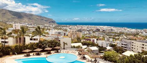 Un resort con una amplia piscina, palmeras y vistas a la ciudad y al océano.