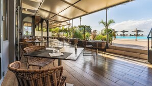 An outdoor dining area with wicker furniture and a view of a pool. - Hôtel Exsel Créolia  (Saint-Denis)