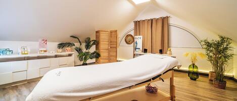 A treatment room with a bed, a counter with products, and plants.