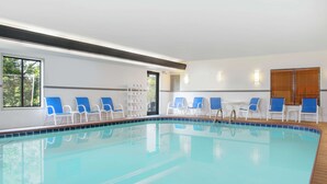 A swimming pool with blue and white lounge chairs, a wooden deck, and a view of the outdoors.