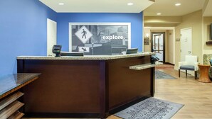 A hotel reception area with a blue wall, a reception desk with a digital kiosk, and a sign that says "explore."