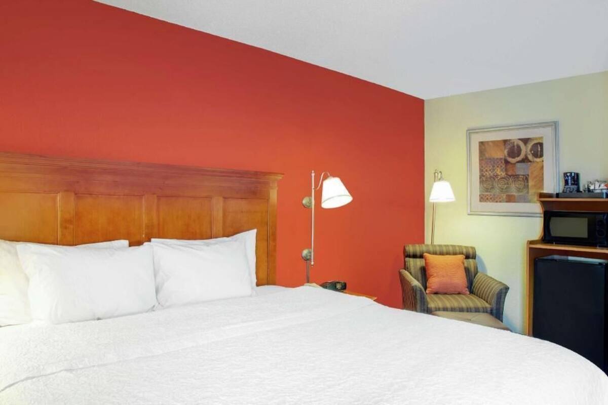 A hotel room with a large bed, a chair, a desk with a lamp, and a microwave.