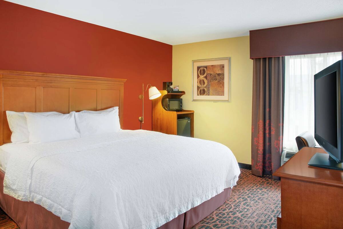 A hotel room with a large bed, a desk with a television, a microwave, and a lamp.
