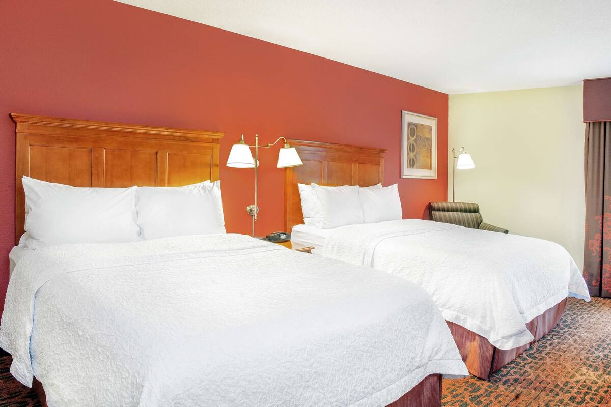 A hotel room with two beds, a wooden headboard, a patterned carpet, and a wall-mounted lamp.