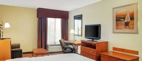 Una habitación de hotel con una cama, un escritorio, una silla, un televisor y un cuadro en la pared.