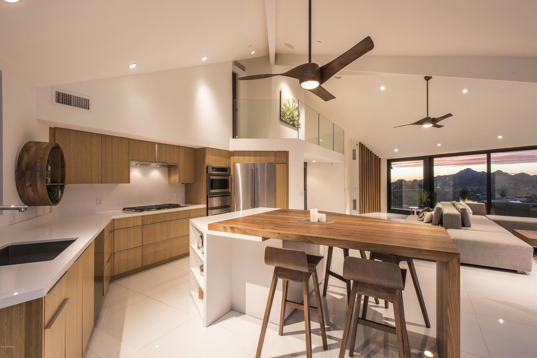 A modern kitchen with a central island, bar stools, and a view of mountains through large windows.