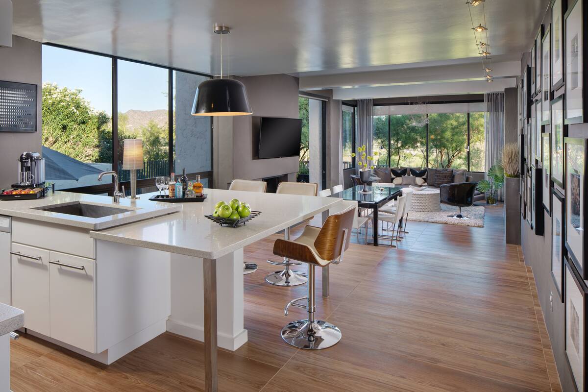 A modern kitchen with a large island, bar stools, and a dining area with a view of the outdoors.