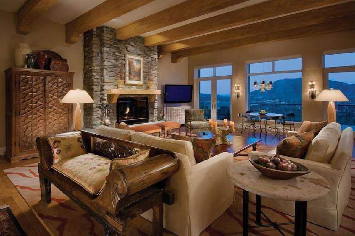 A spacious living room with a stone fireplace, comfortable seating, and large windows offering a view of the mountains.